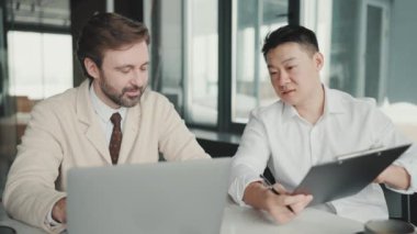 Meditative multinational colleagues talking about project and looking at laptop in the office