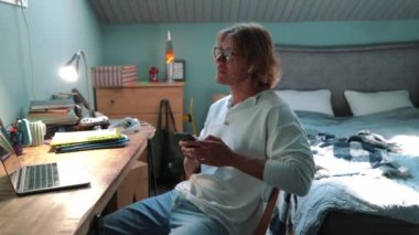 Cheerful blond man typing on mobile at home indoors