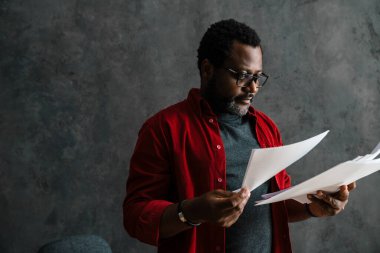 Black bearded man in eyeglasses working with papers indoors