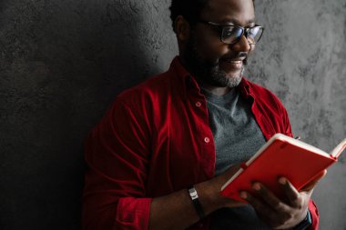 Black man in eyeglasses writing down notes while leaning on concrete wall