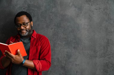 Black man in eyeglasses writing down notes while leaning on concrete wall