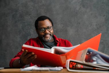 Black man in eyeglasses working with papers while sitting at desk indoors