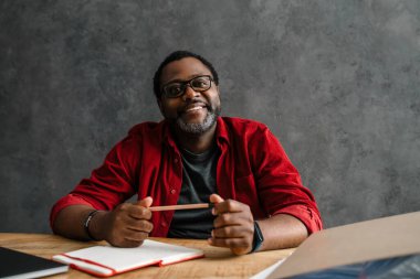 Black man in eyeglasses working with laptop while sitting at desk indoors