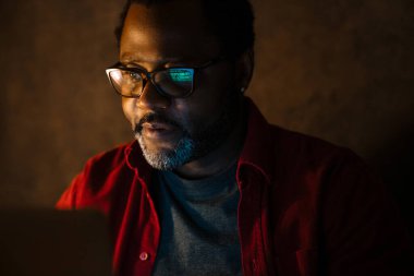 Black bearded man in eyeglasses working with laptop indoors