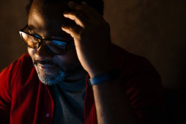 Black bearded man in eyeglasses posing and looking aside indoors