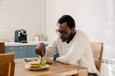 Black man wearing eyeglasses drinking coffee while having dinner at home