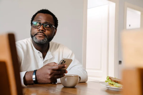 Black Man Wearing Eyeglasses Using Mobile Phone While Having Dinner — Stockfoto