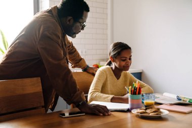 Black girl smiling while doing homework with her father at home