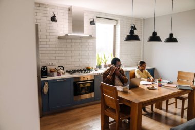 Black man talking on cellphone while his daughter doing homework at home