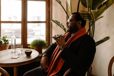 Black man talking on cellphone while drinking coffee in cafe indoors