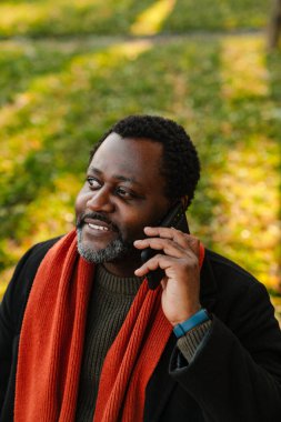 Black bearded man talking on cellphone while strolling at park