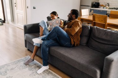 Black girl making fun with her father while sitting on sofa at home