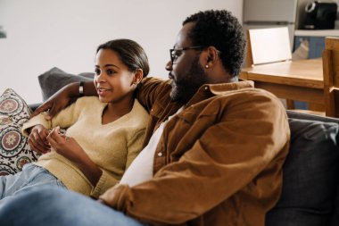 Black girl talking and smiling with her father while sitting on sofa at home