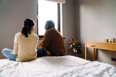 Black girl and her father talking while sitting on bed at home