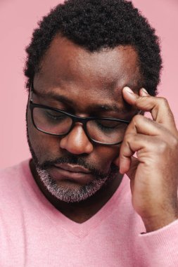 Black puzzled man in eyeglasses thinking with eyes closed isolated over pink background