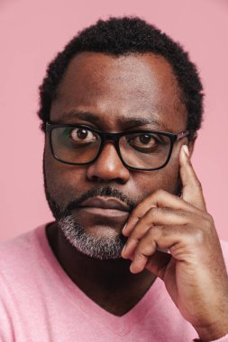 Black puzzled man in eyeglasses thinking while looking at camera isolated over pink background