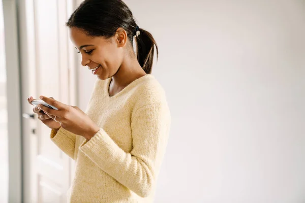 Black Brunette Girl Using Mobile Phone While Standing Home — Stockfoto