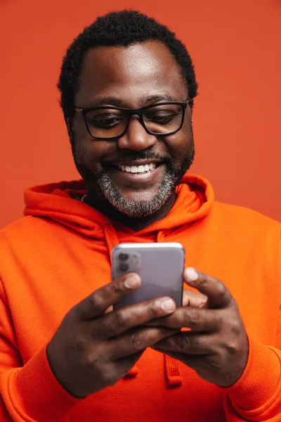 Black Bearded Man Eyeglasses Smiling Using Cellphone Isolated Orange Background — Stockfoto