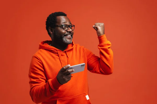 Black Bearded Man Making Winner Gesture Using Cellphone Isolated Orange — Stockfoto