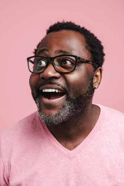 Black bearded man in eyeglasses expressing surprise at camera isolated over pink background