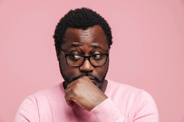 Black puzzled man in eyeglasses posing and looking aside isolated over pink background