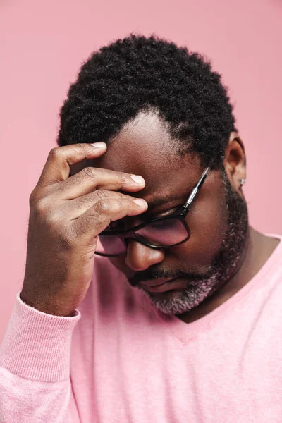 Black puzzled man in eyeglasses thinking while holding his head isolated over pink background