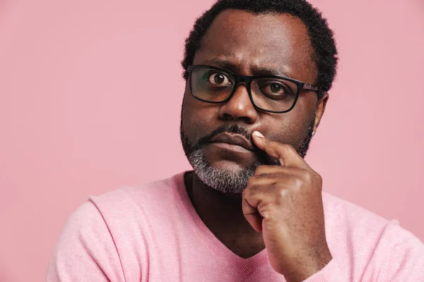 Black puzzled man in eyeglasses thinking while looking at camera isolated over pink background