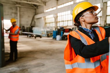 Multiracial man and woman in protective clothing working with equipment at factory