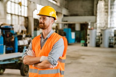 White ginger man wearing helmet and vest working at factory