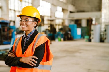 Black woman wearing helmet and vest smiling while working at factory