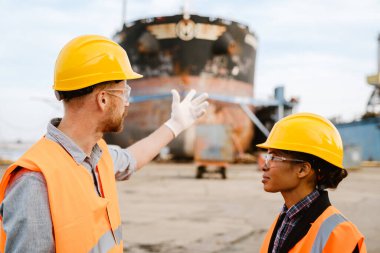 Multiracial man and woman in protective clothing talking while working at port