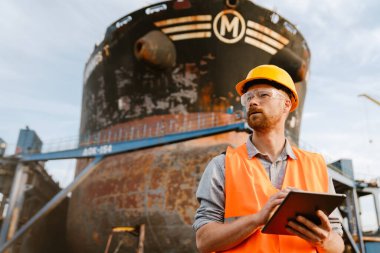 White man wearing helmet and vest using tablet computer while working in port