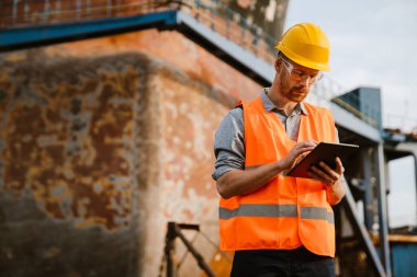 White man wearing helmet and vest using tablet computer while working in port