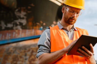 White man wearing helmet and vest using tablet computer while working in port