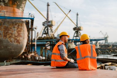 Multiracial man and woman wearing helmets working together at port