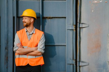 White ginger man wearing helmet and vest laughing while working in port