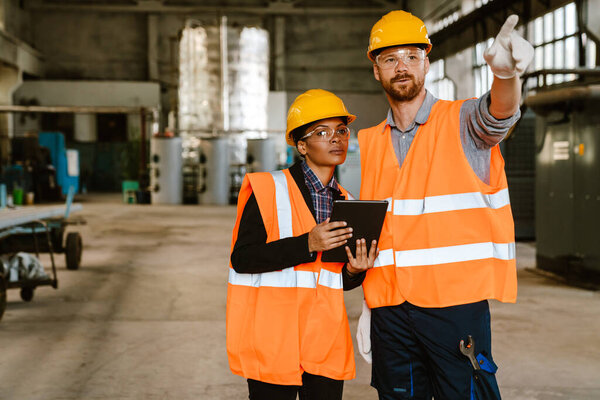Multiracial man and woman in protective clothing working with tablet computer at factory