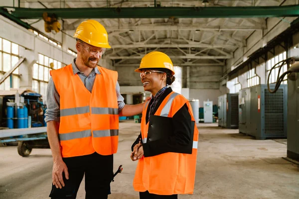 Multiracial man and woman in protective clothing talking while working at factory