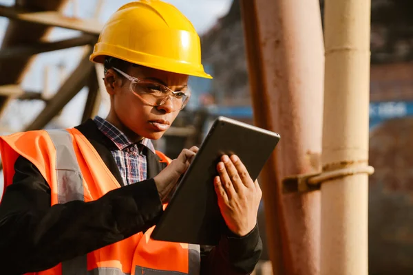 Black woman wearing helmet and vest working with tablet computer in port