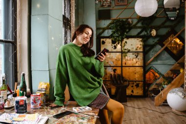 Young white woman using cellphone while working in her studio
