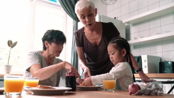 Smiling Mature Lesbian Couple Eating Breakfast Adopted Asian Daughter Kitchen — Vídeo de stock