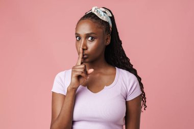 Black surprised woman with pigtails showing silence gesture isolated over pink wall