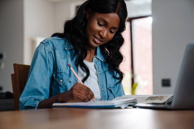 Black young woman using laptop while doing homework at home