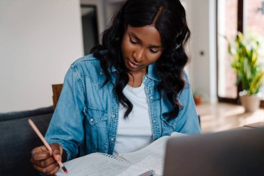 Black young woman using laptop while doing homework at home