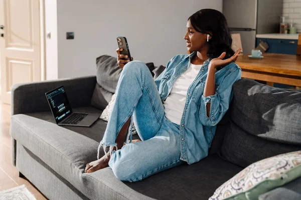 Black Young Woman Earphones Using Mobile Phone While Sitting Couch — Stockfoto