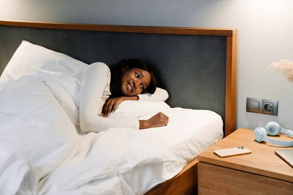 Μαύρη Νεαρή Γυναίκα Χαμογελά Ενώ Βρίσκεται Λευκό Κρεβάτι Λινό Στο — Φωτογραφία Αρχείου