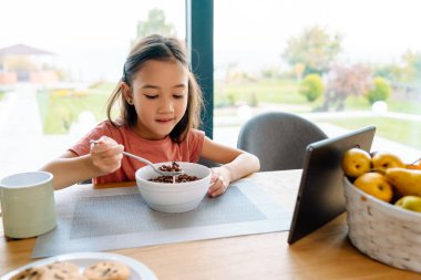Asian girl using tablet computer while having breakfast at home