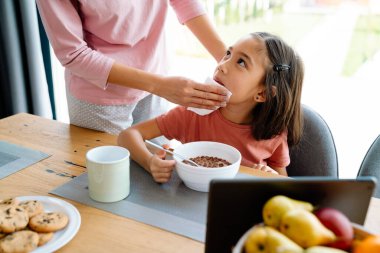 Asian girl using tablet computer while having breakfast with her mother at home