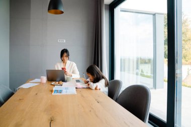 Asian woman working with laptop while her daughter doing homework at home