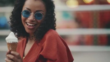 Cheerful hispanic woman wearing sunglasses posing with ice cream in adventure park